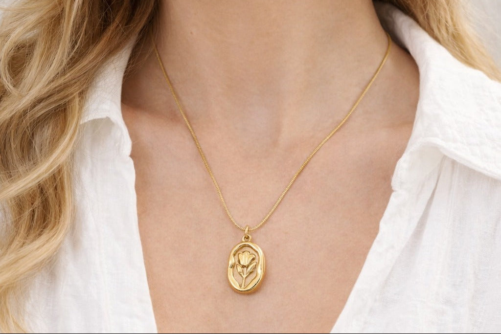 Gold necklace with a pendant worn by a person with blonde hair and a white shirt.